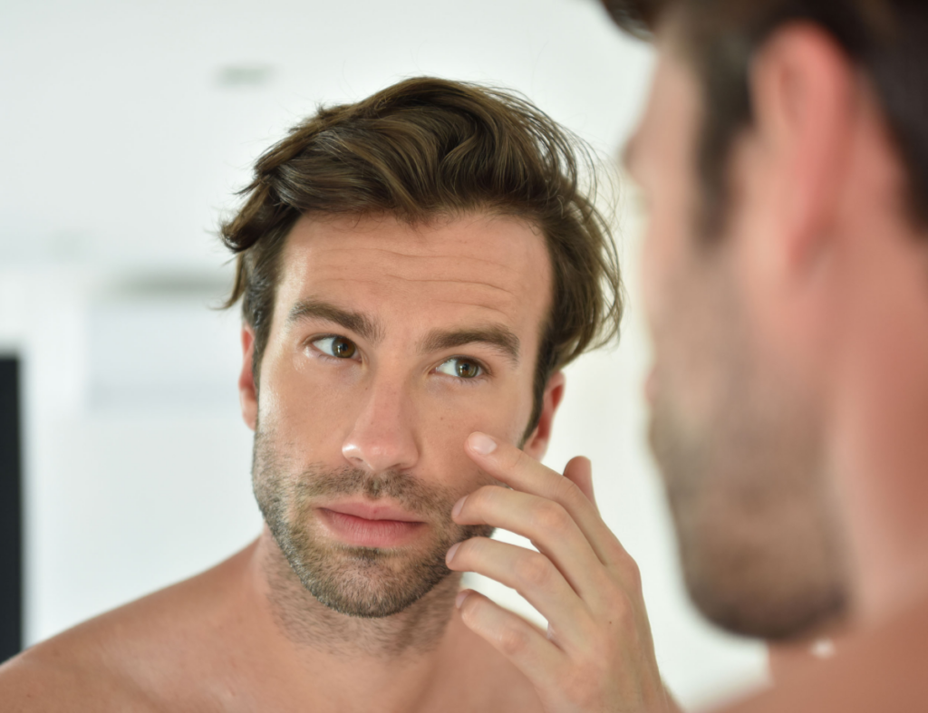 A man looking to the mirror while touching his face